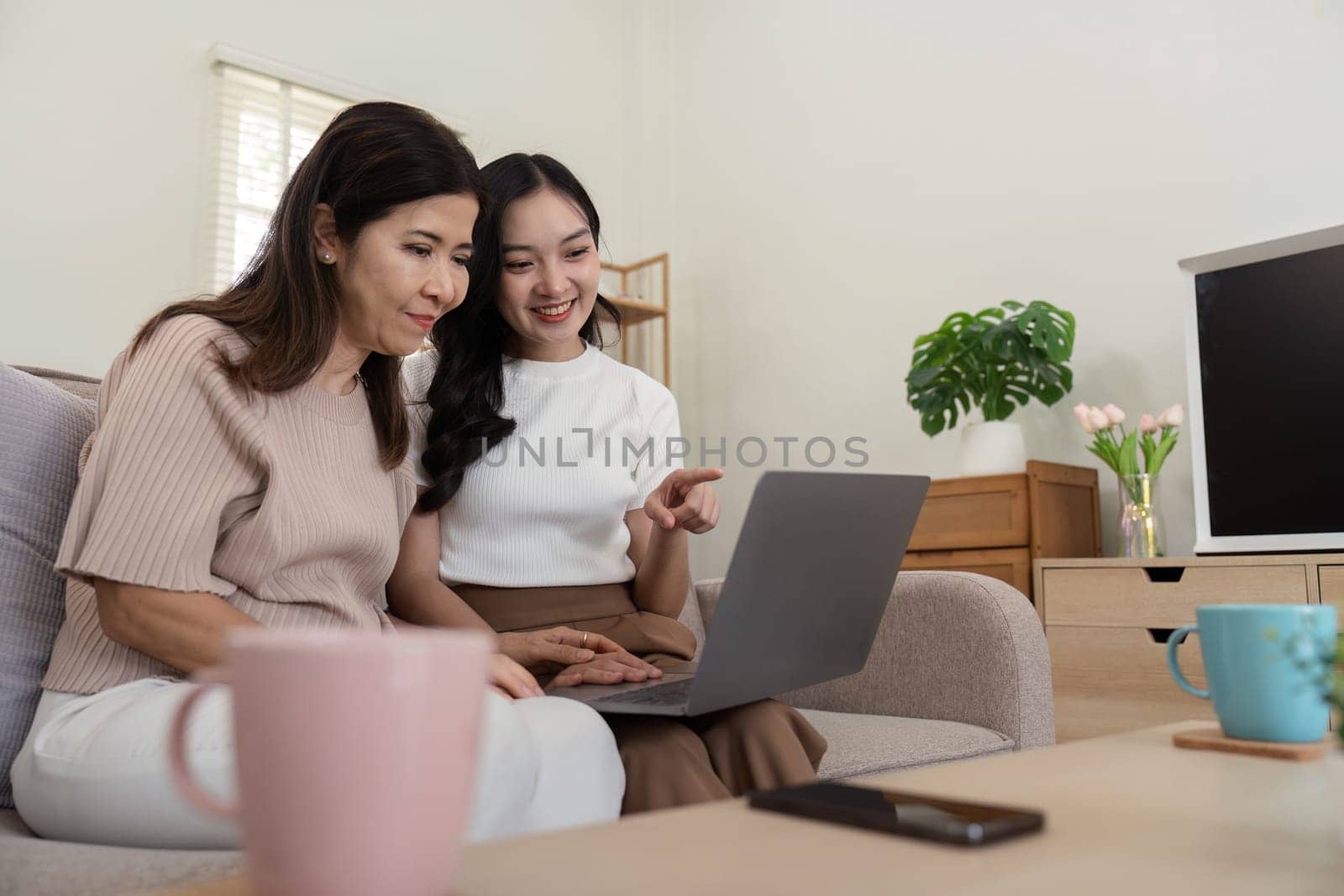 Mother and beautiful young grownup daughter using online app on laptop, watching movie, interactive TV channel. spending leisure time together at home.