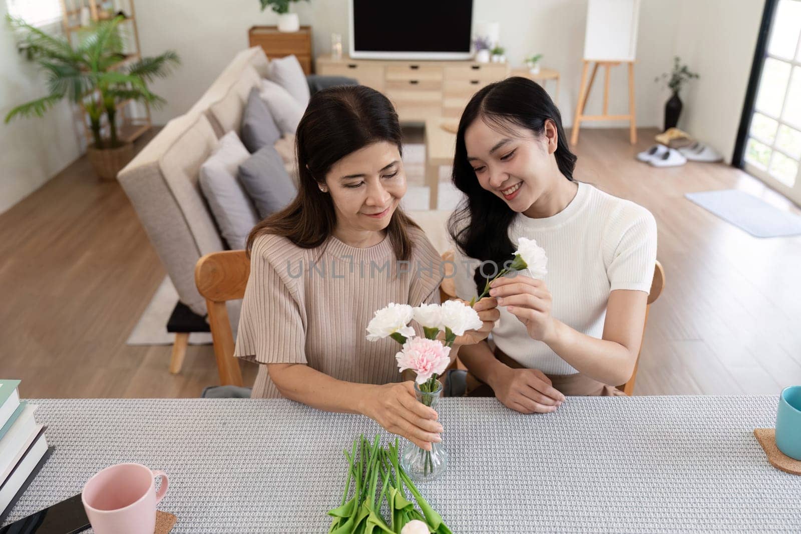 Senior mother and adult daughter happy on the table while arrange flowers in a vase together. Technology and lifestyle concept. Happy time together by nateemee