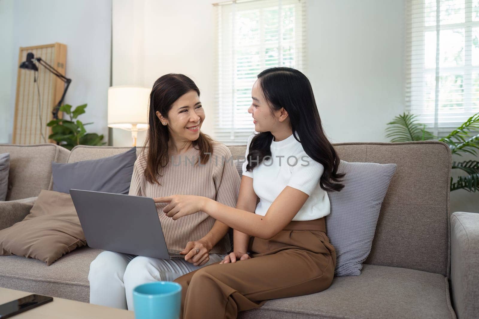 Mother and adult daughter sitting on the sofa together, mother and daughter using laptop to surf website together.