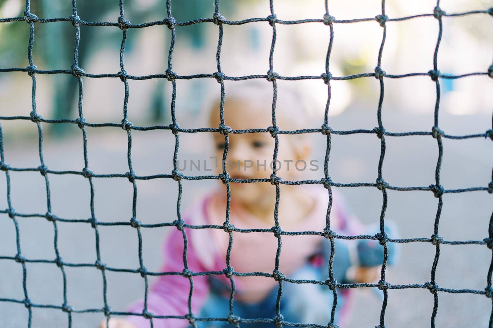 Little girl with a toy sat down behind the net. Blur. High quality photo