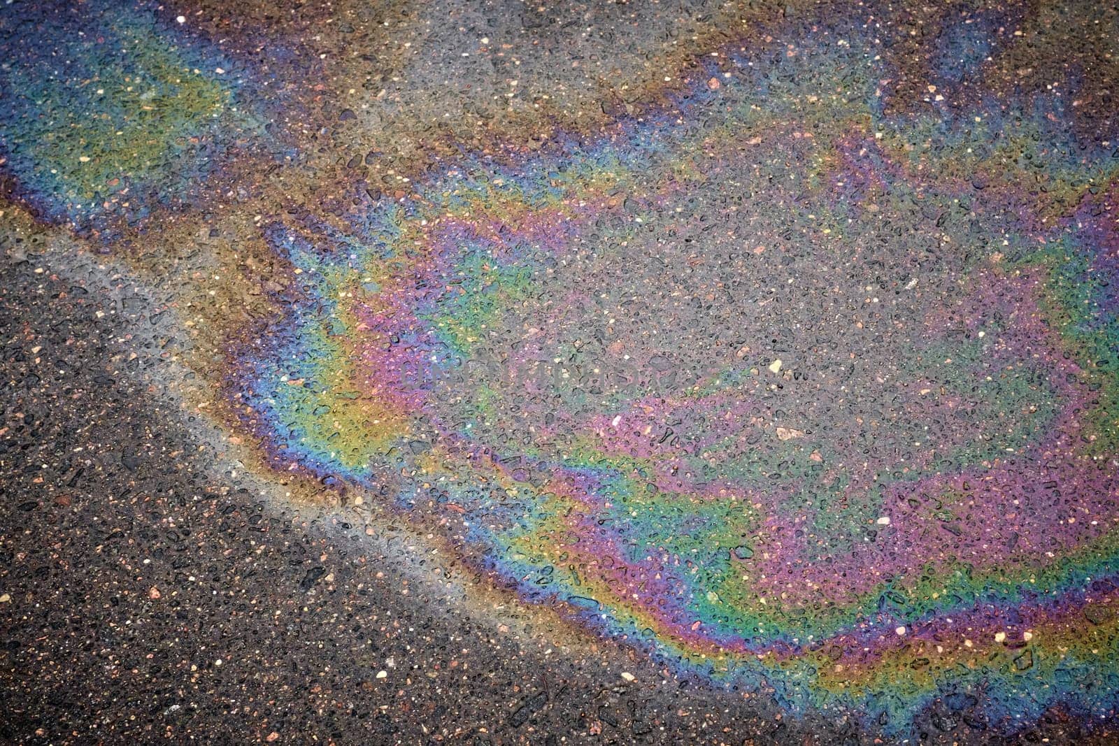 Detailed stain of fuel or oil on wet asphalt during a rainy day, emphasizing environmental pollution.