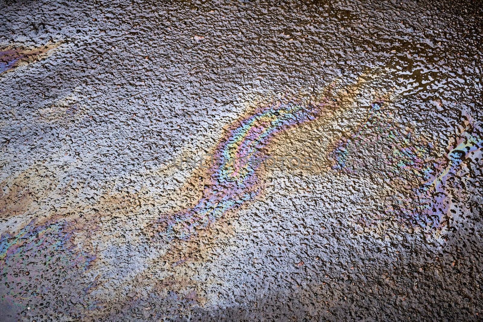 Oil stains from leaks in the car engine. Oil after rain makes spots with rainbow reflections refractive sun spectrum