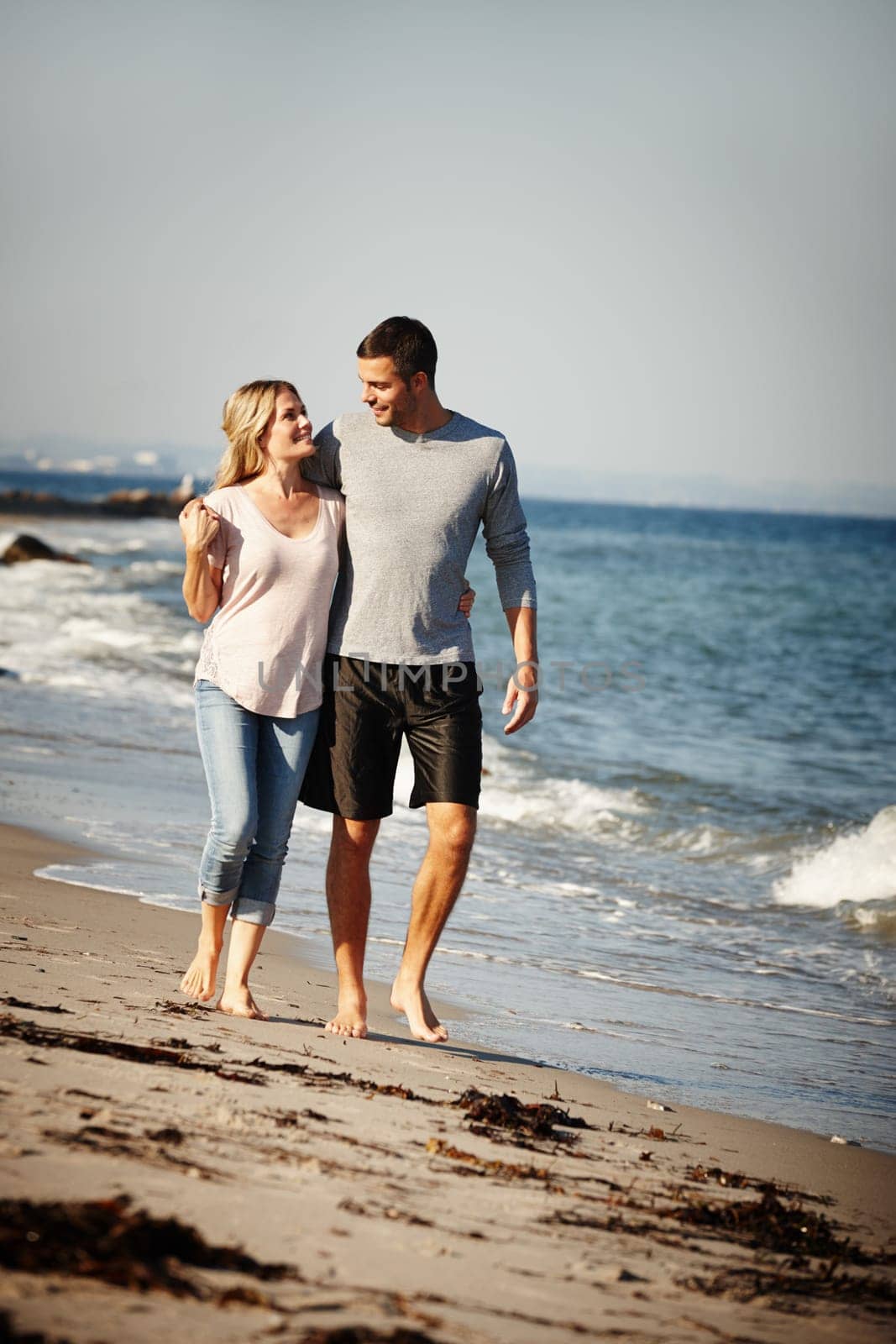Couple, walking and hug on sand of beach, peace and travel to nature for holiday. People, embrace and calm on weekend trip or vacation, love and date for relationship or marriage and ocean waves.