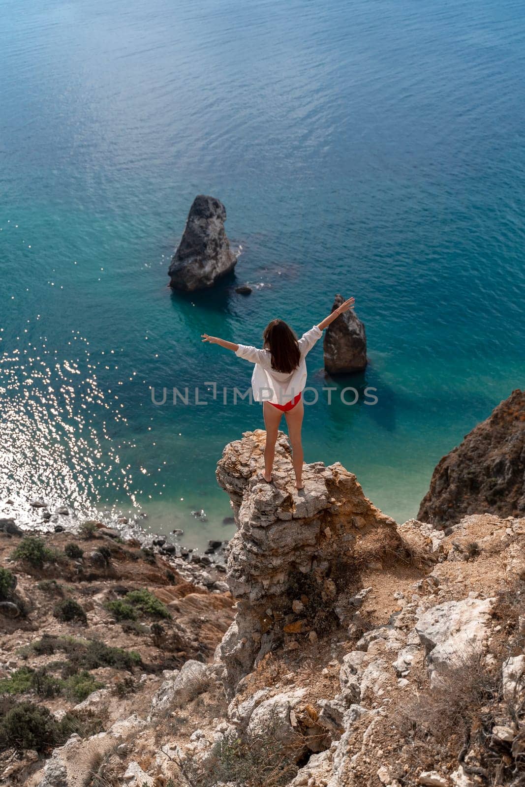 A woman is standing on a rock overlooking the ocean. She is enjoying the view