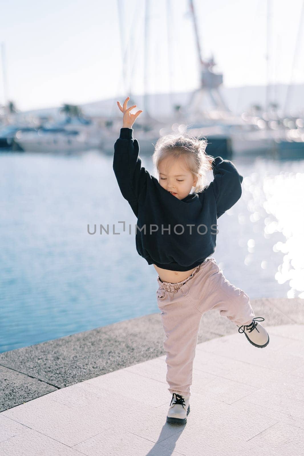 Little girl dancing waving her arms and legs on the embankment. High quality photo