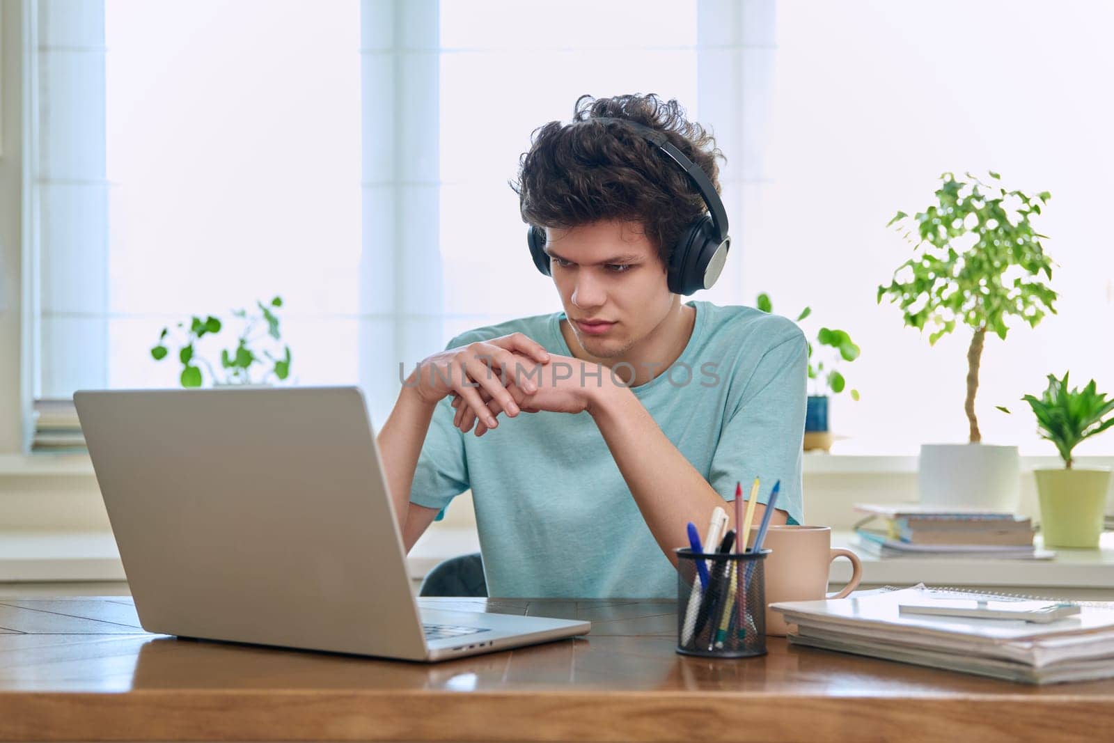 Young guy college student in headphones looking at web cam computer laptop, talking, studying online, sitting at home at desk. E-learning, remote training, education, youth, technology concept