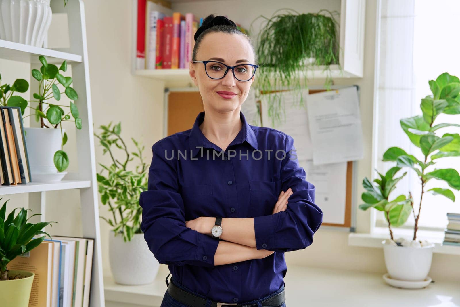 Portrait of beautiful confident woman 40 years old wearing glasses with crossed arms looking at camera in home interior