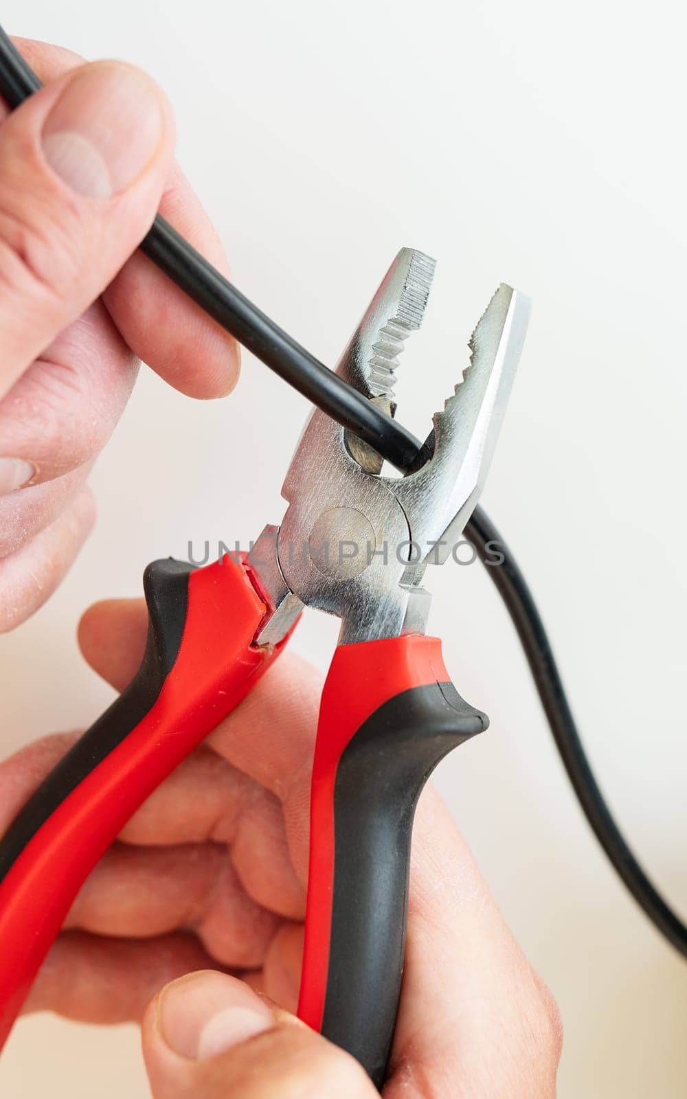Close-up of hands using pliers to cut a black wire, highlighting a DIY electrical repair task