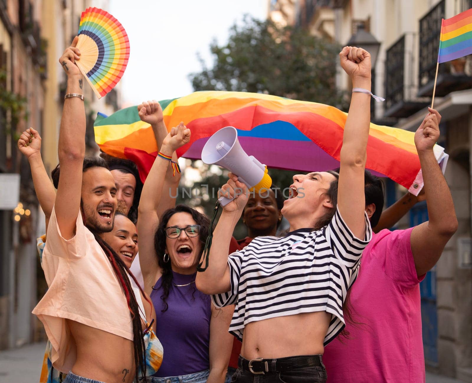 Group of LGBTQ people are holding rainbow flags and a megaphone during MADO party chueca pride gay day.