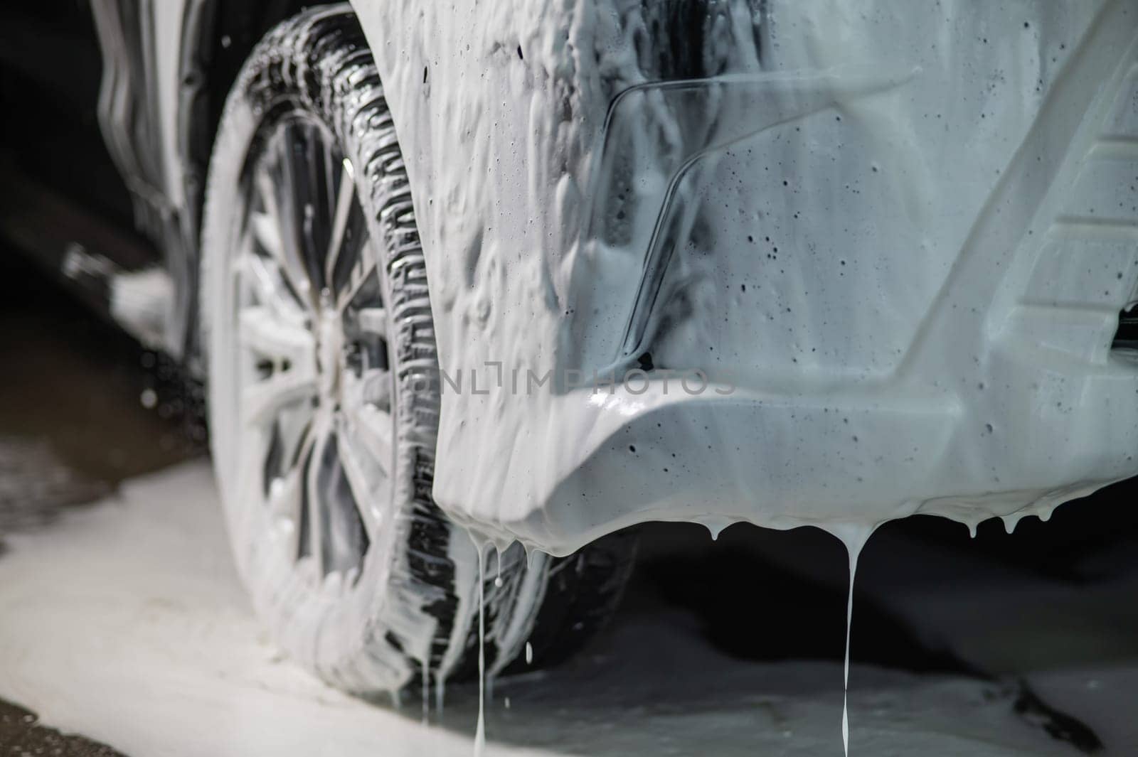 Foam drips from the bumper of a black car. Car wash