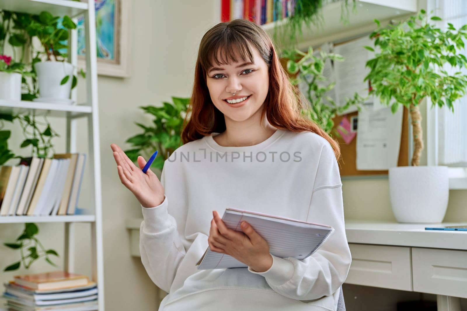 Web camera view of teenage student girl with notebook looking at camera at home. Online lesson video chat call conference. Technology education training e-learning concept