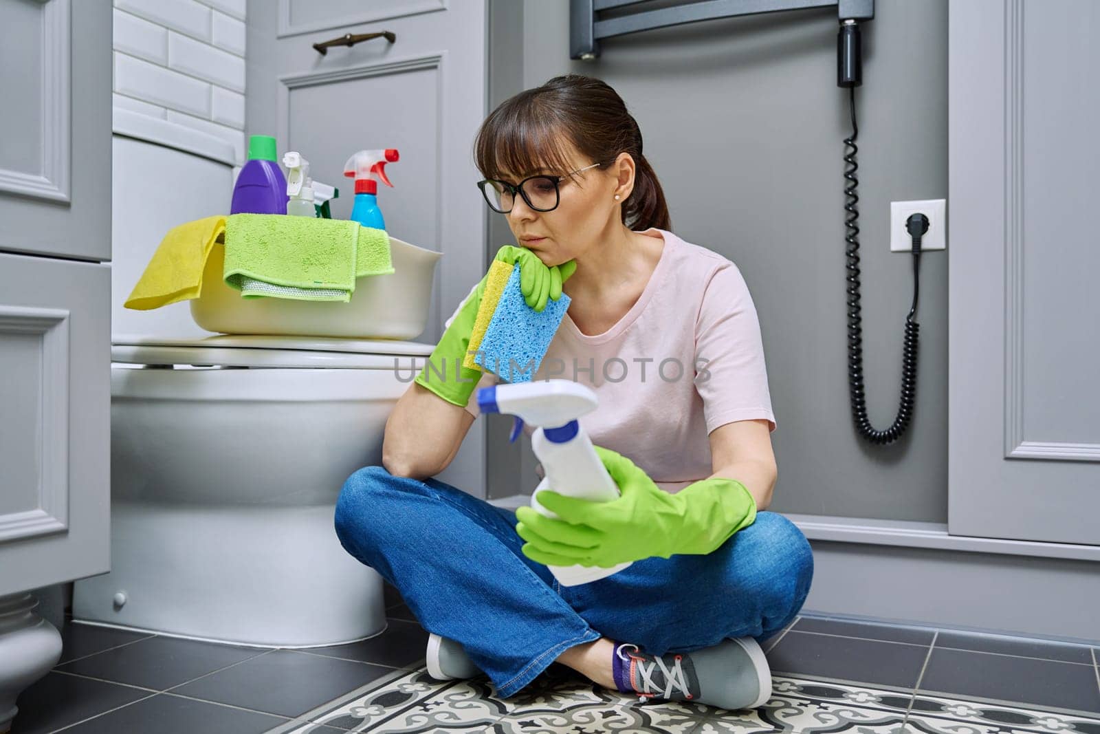 Tired woman sitting on the floor after cleaning bathroom, toilet. Routine house cleaning, home hygiene, housecleaning service, housekeeping, housework