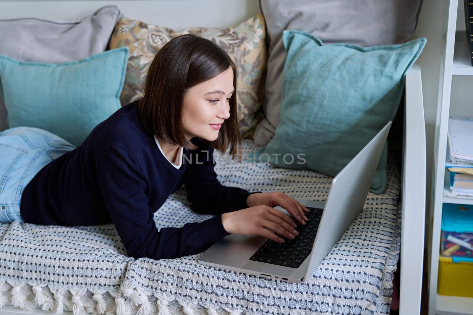 Young woman using laptop lying on sofa at home by VH-studio