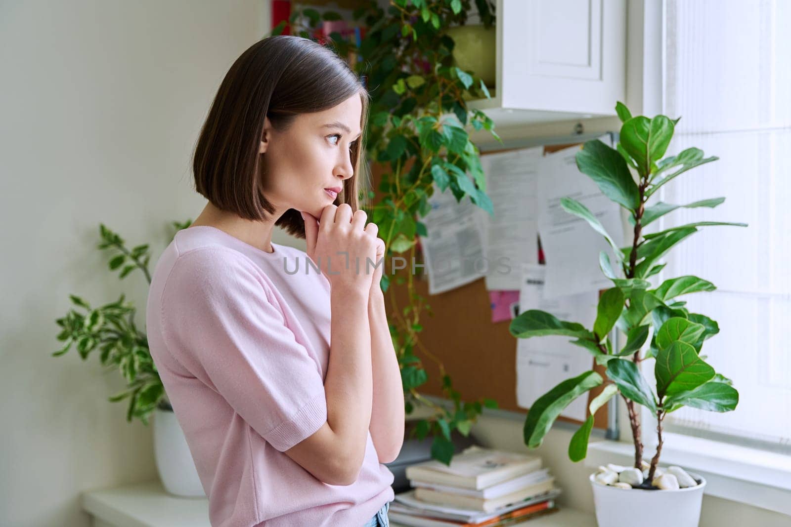 Serious young woman looking out the window, in home interior by VH-studio