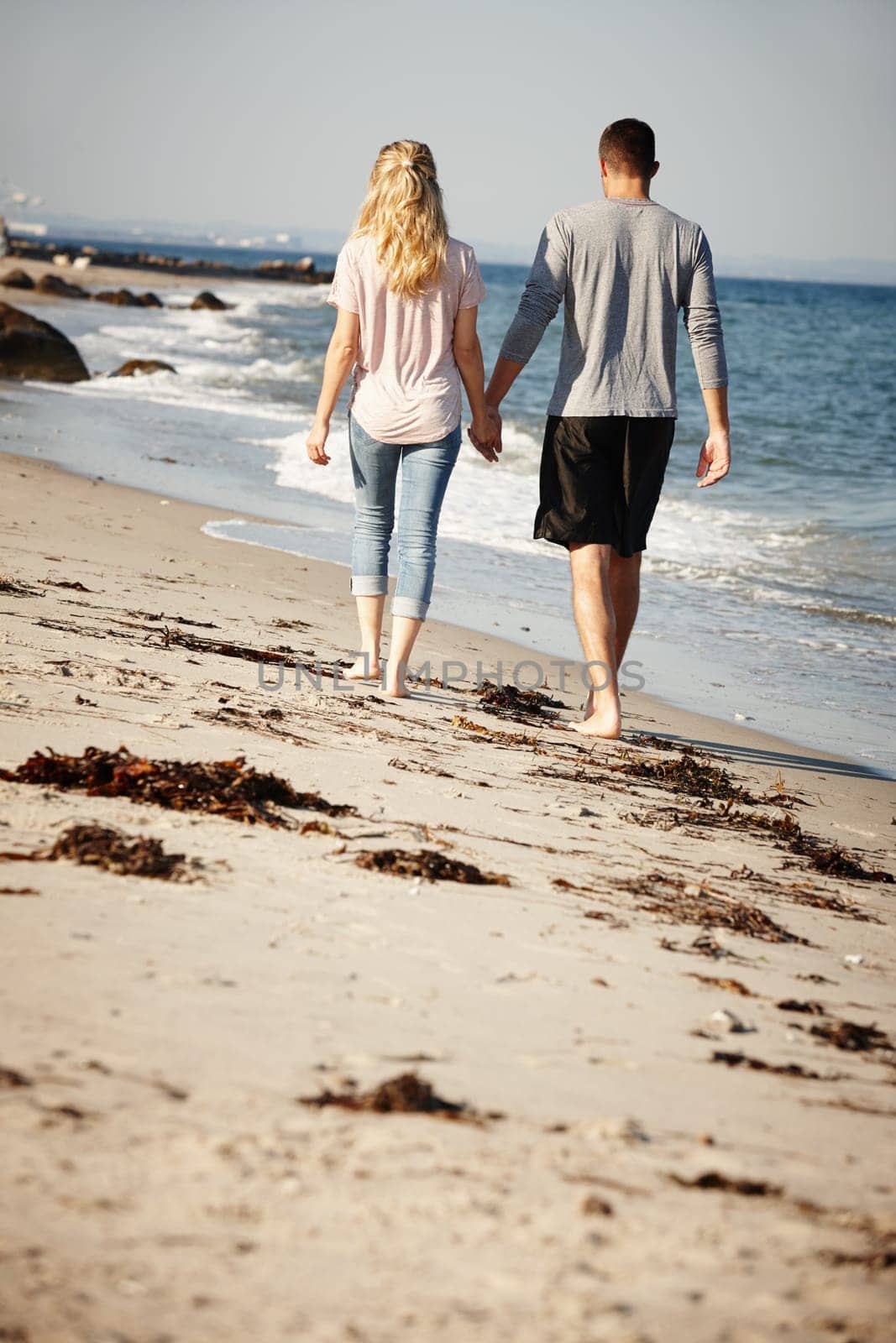 Couple, walking and holding hands on sand of beach, peace and travel to nature for holiday. People, back and calm on weekend trip or vacation, love and date for relationship or marriage and ocean.