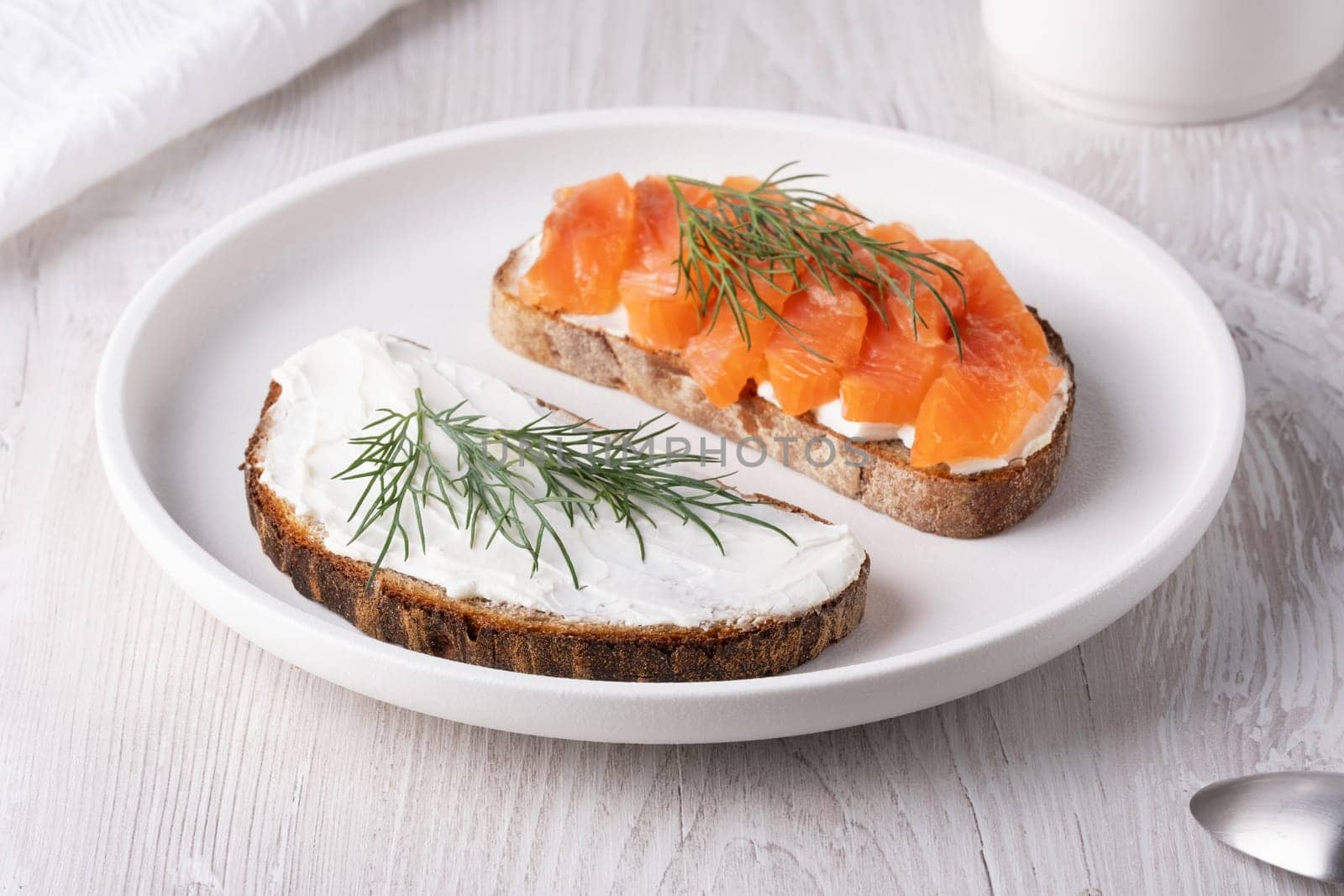 Rye sandwich with salmon and cream cheese on white wooden table.