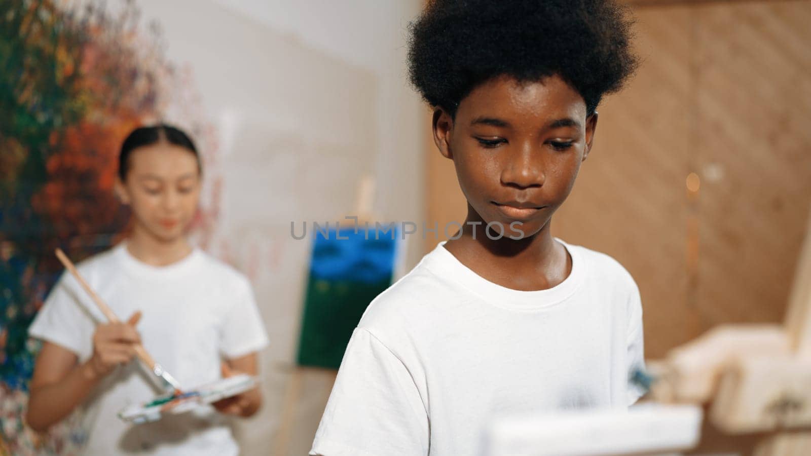 Diverse children in casual shirt painting canvas together in creative art lesson. Multicultural happy highschool student drawing a same canvas while standing at colorful stained wall. Edification.