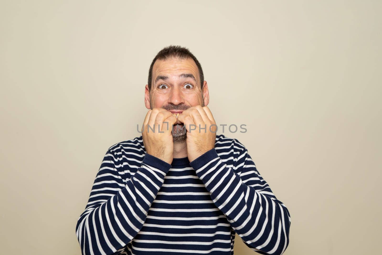 Hispanic man in his 40s standing over isolated beige background looking stressed and nervous with hands on mouth biting nails. Anxiety problem by Barriolo82