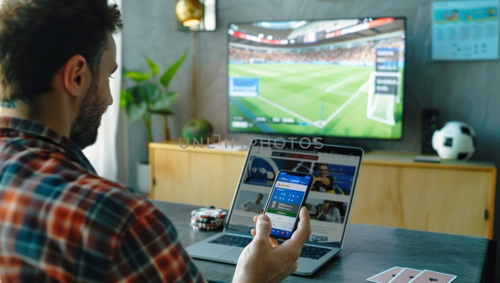 Rear view of a man that watches soccer match on television and bets on the game with betting app on phone.