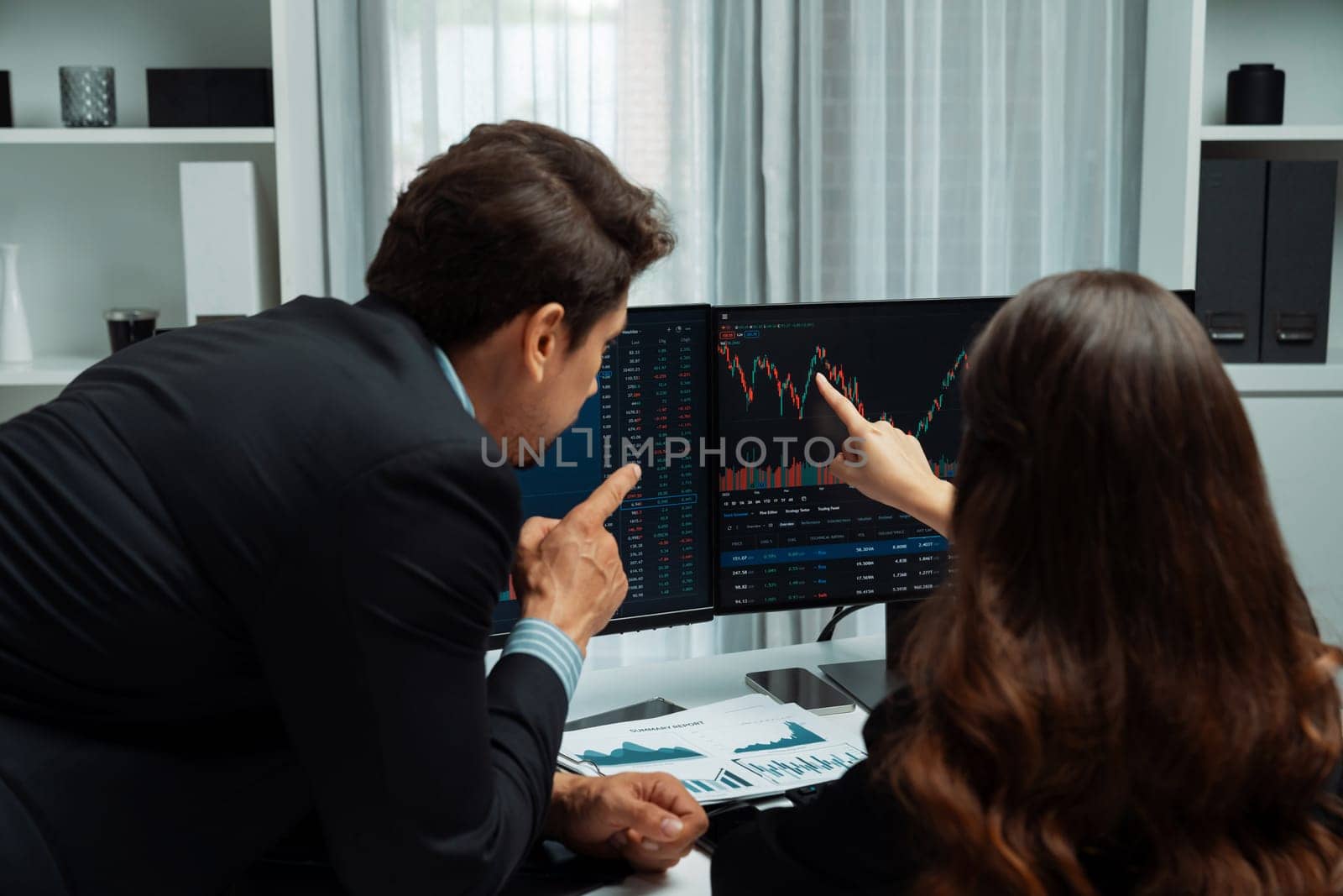 Two business traders discussing on dynamic stock market in currency rate investment trading on two pc screens with compare real time graph on risk or profit point of data at modern office. Postulate.