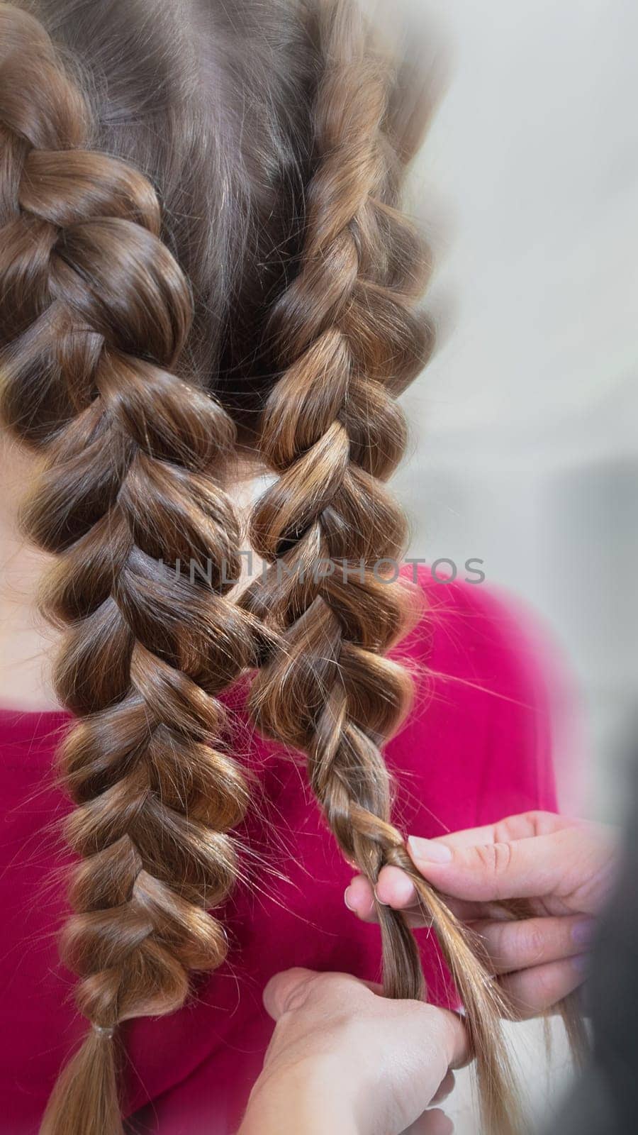 Hairdresser weaves a braid to a preteen blond girl in a beauty and hair salon with motion blur effect by Mariakray