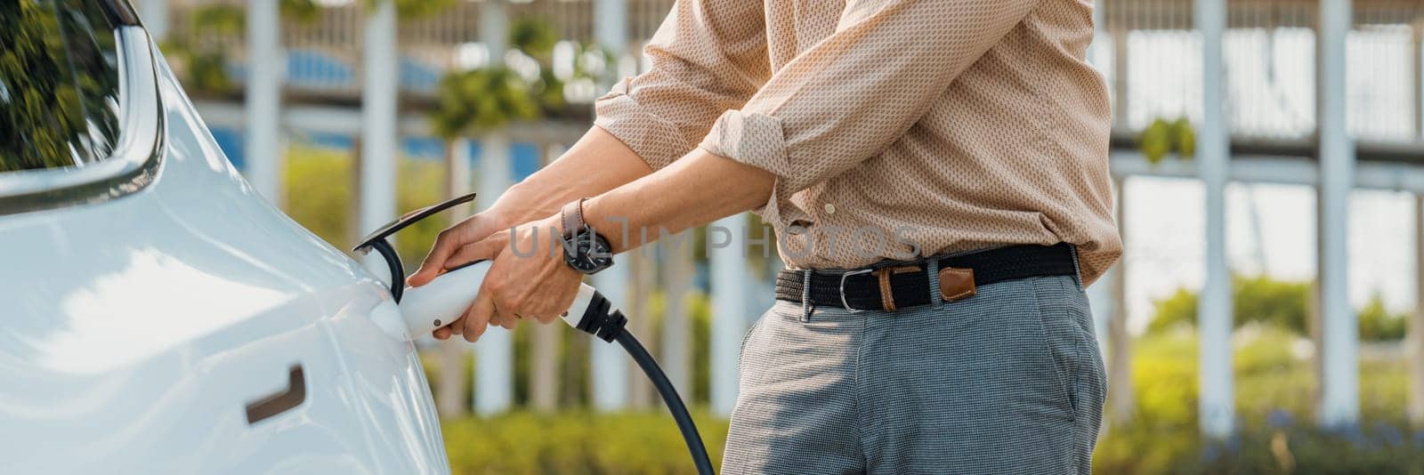 Young man recharge electric car's battery from charging station. Expedient by biancoblue