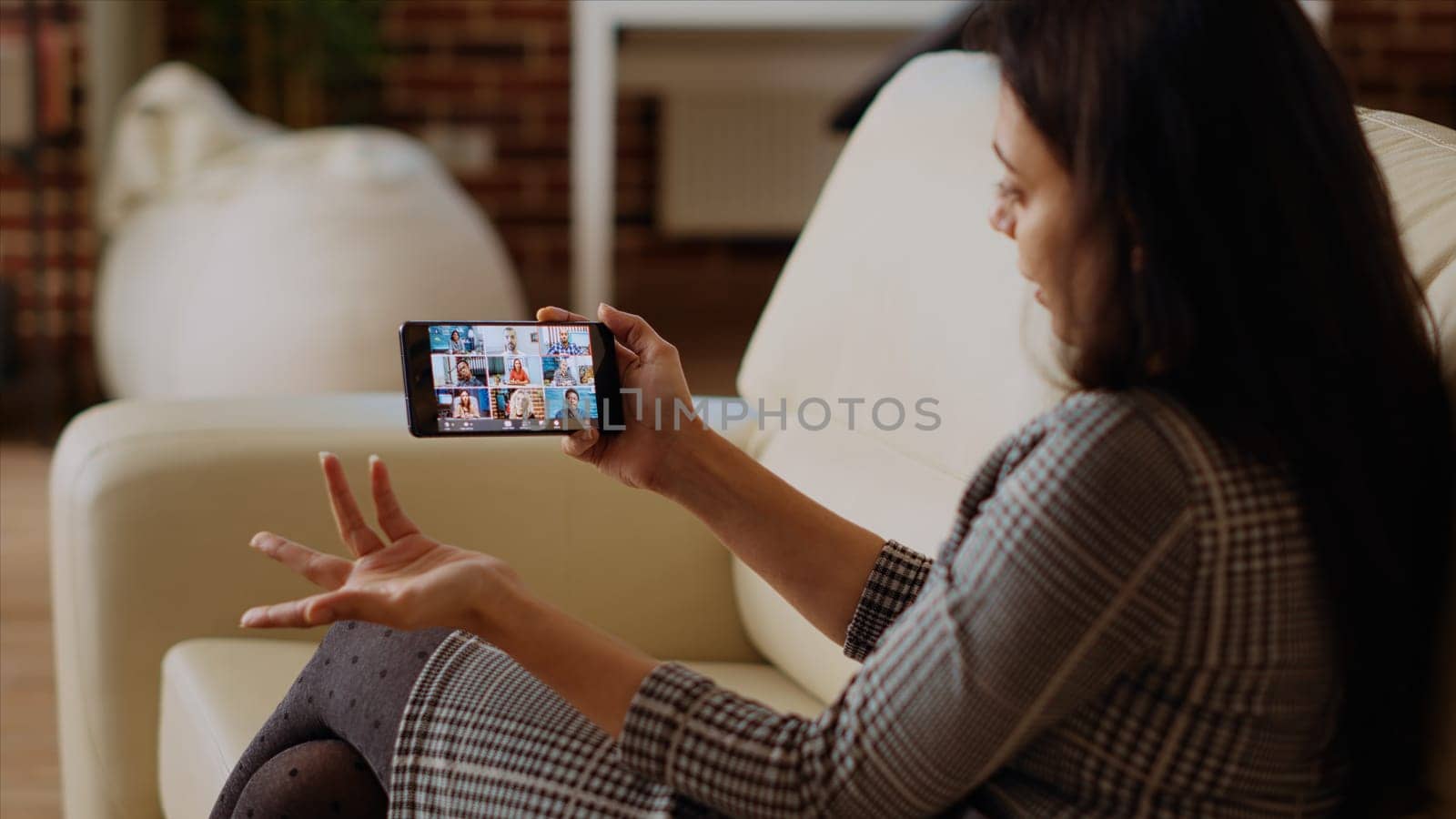 Management executive using smartphone to delegate project tasks to employees during videoconference meeting. Manager at home holding internet videocall on phone with diverse team