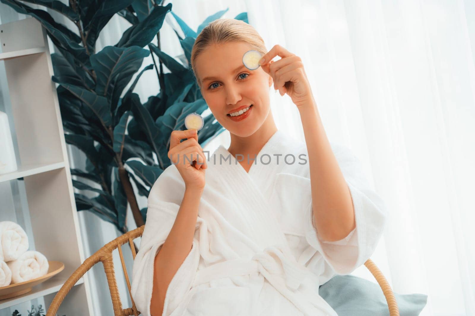 Woman holding slices of fresh cucumber and wearing bathrobe enjoying luxurious facial skincare spa in resort or hotel. Skin treatment for face and beauty care. Quiescent