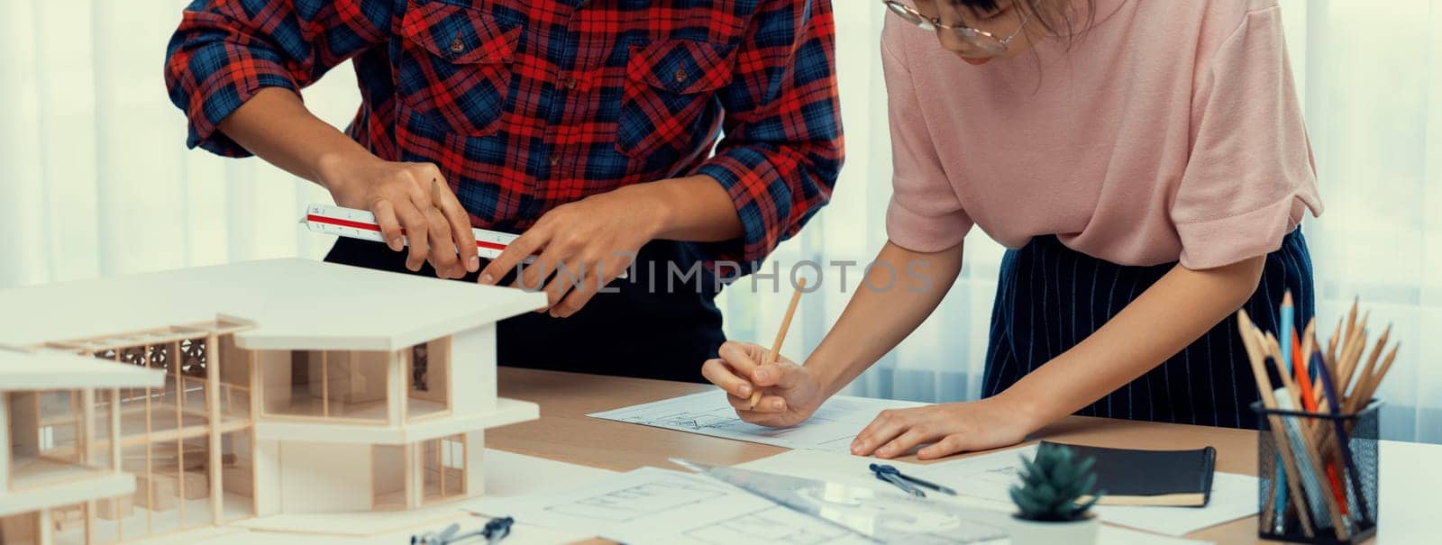 Smart architect engineer and interior designer working together and measuring house model by using ruler on meeting table with blueprint and architectural equipment. Teamwork concept. Burgeoning.