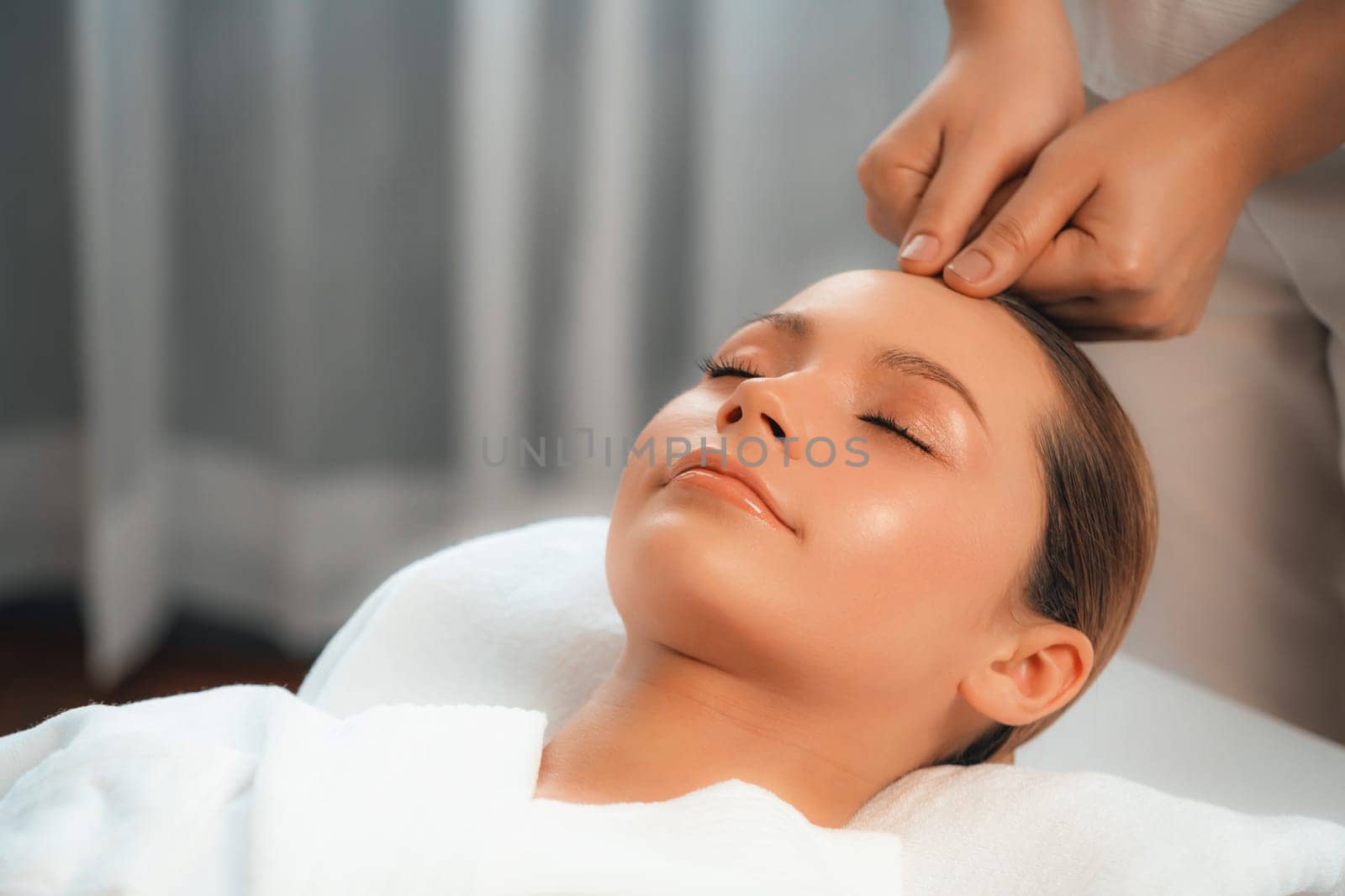 Caucasian woman enjoying relaxing anti-stress head massage and pampering facial beauty skin recreation leisure in dayspa modern light ambient at luxury resort or hotel spa salon. Quiescent