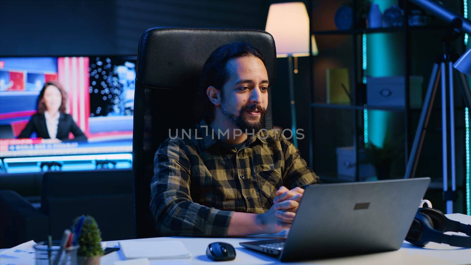 Smiling man relaxing in cozy living room by watching funny internet clips on laptop. Carefree caucasian person enjoying leisure time in RGB lit apartment, looking at online videos, camera A