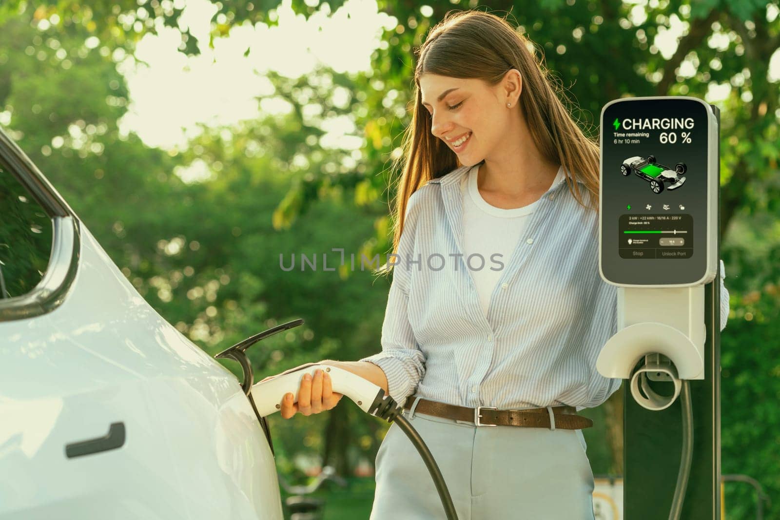 Young woman recharging battery for electric car during road trip. Exalt by biancoblue