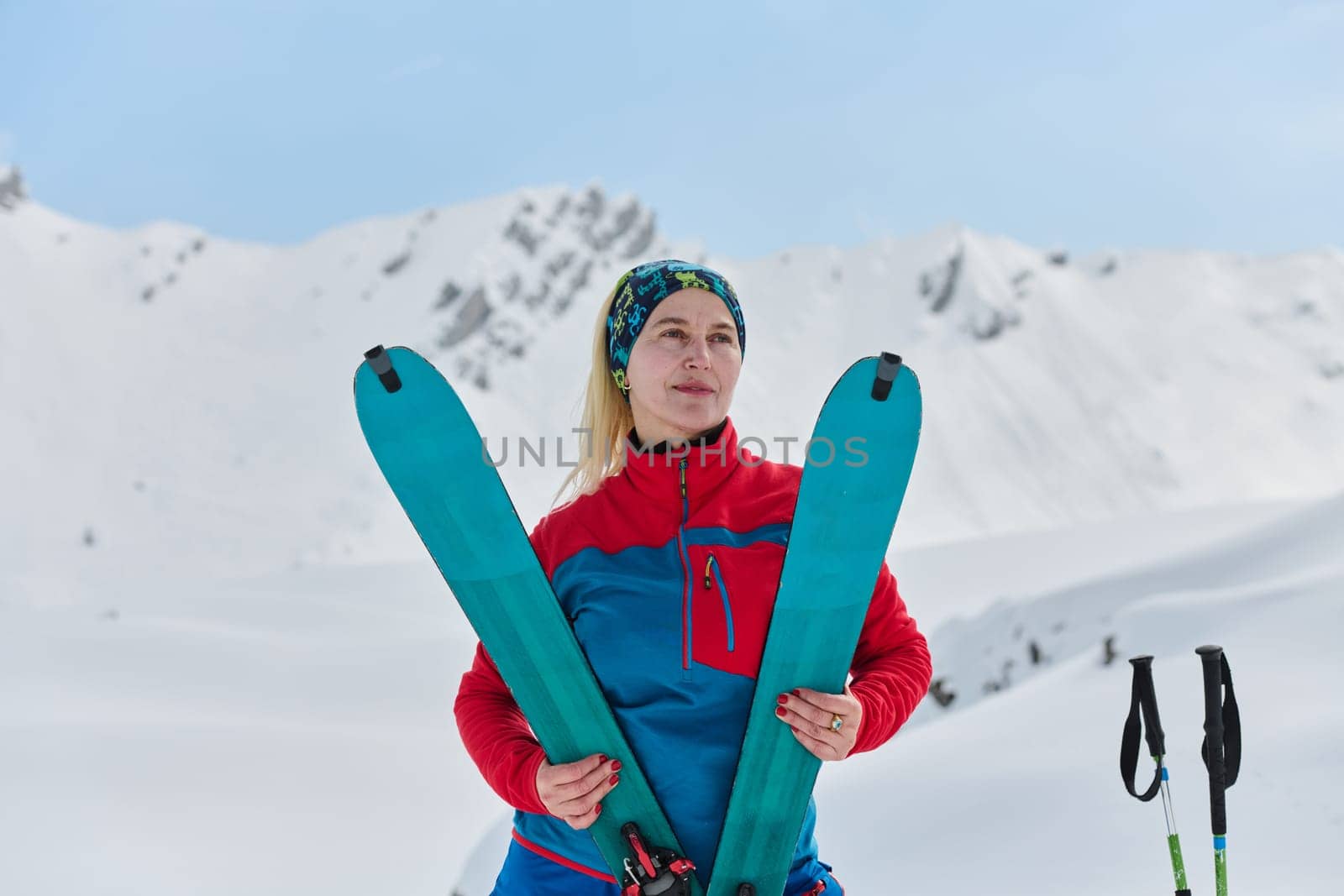 A triumphant female skier beams with confidence atop a snow-capped peak after conquering a challenging ascent.