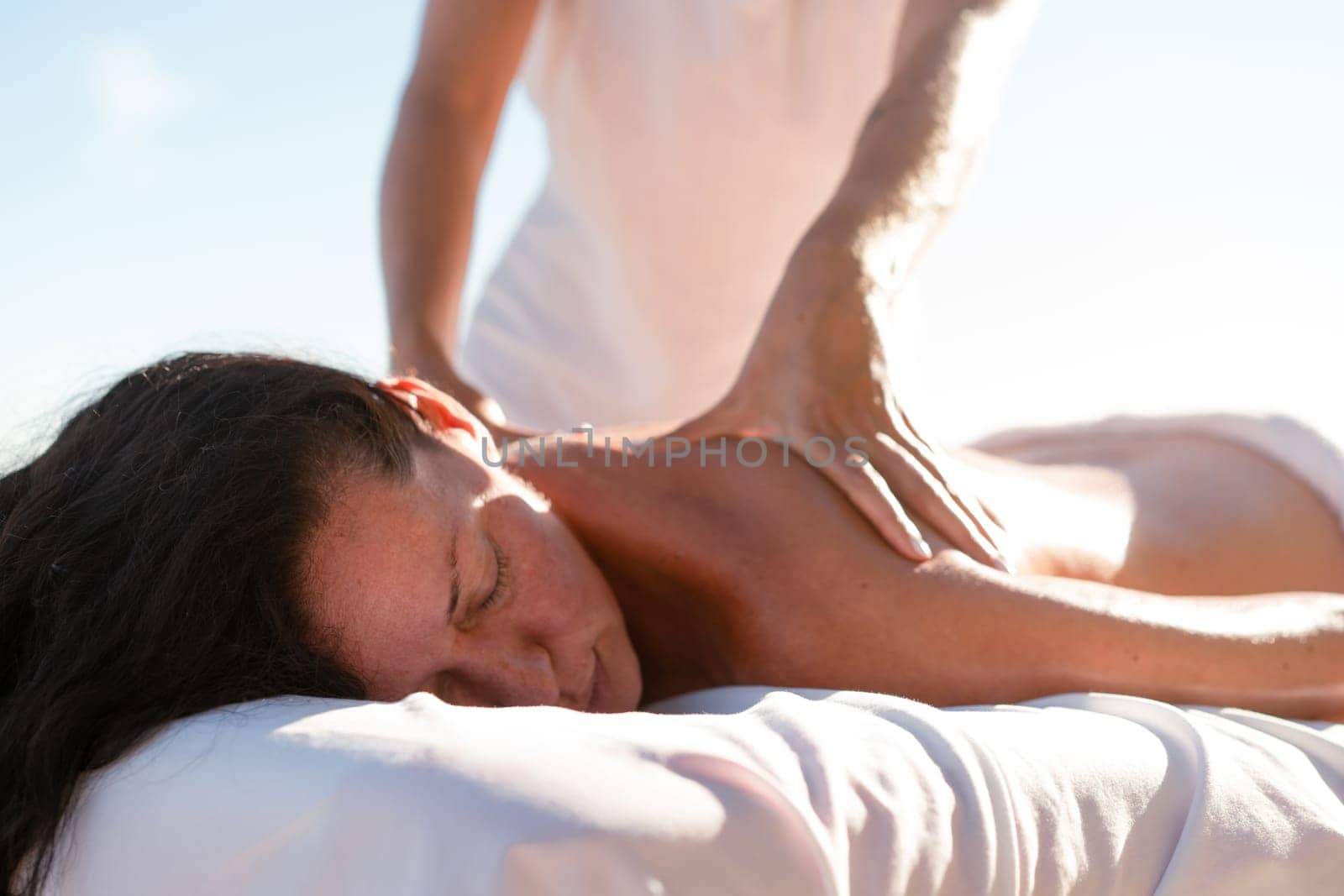 Female masseur massages client's legs on ocean shore by andreonegin
