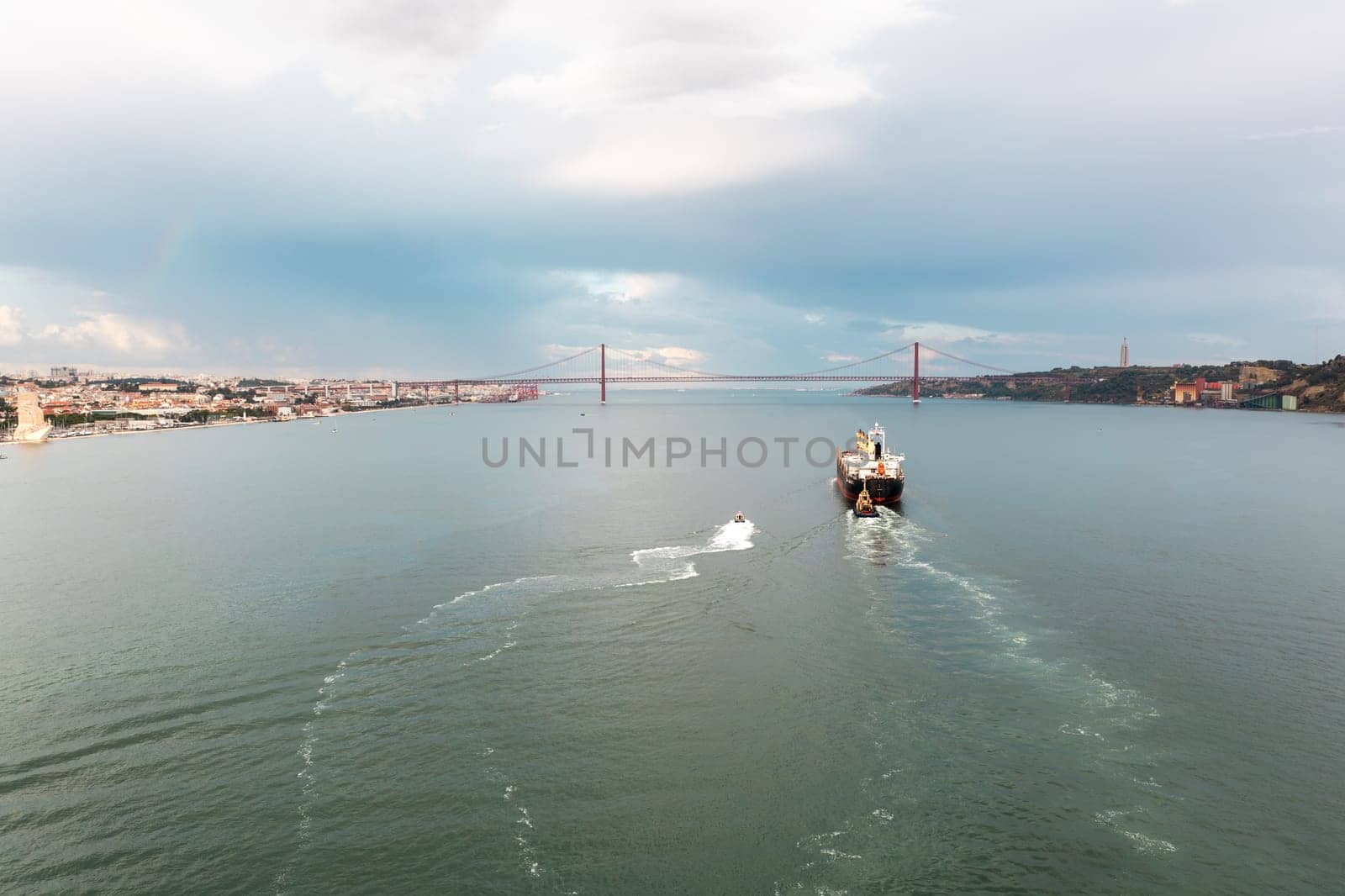 Merchant ship moving on Tagus river with 25 de Abril Bridge in background by andreonegin