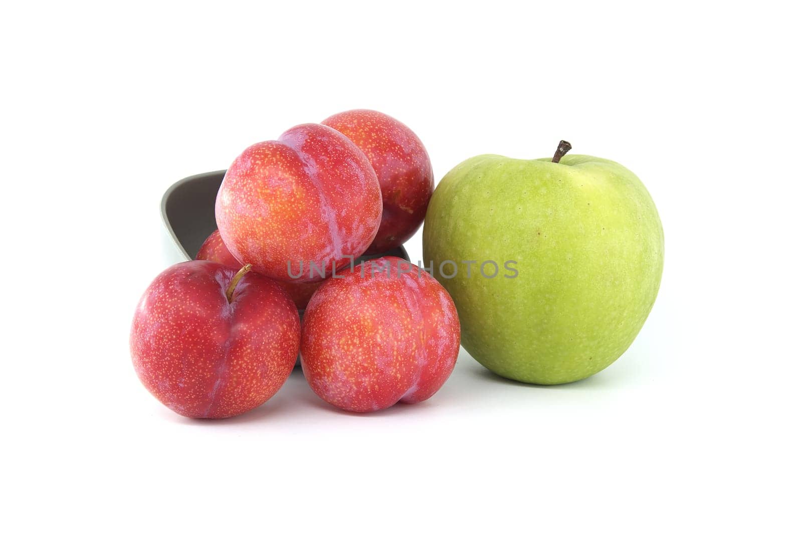 Collection of fresh fruits comprising red plums and bright green apple arranged against a white background