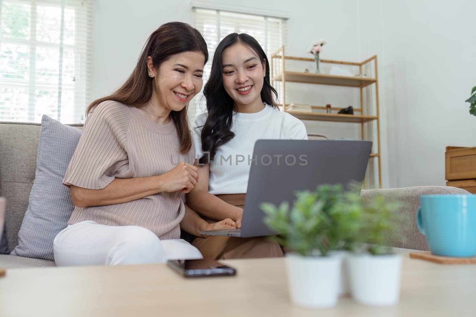 Mother and adult daughter sitting on the sofa together, mother and daughter using laptop to surf website together.