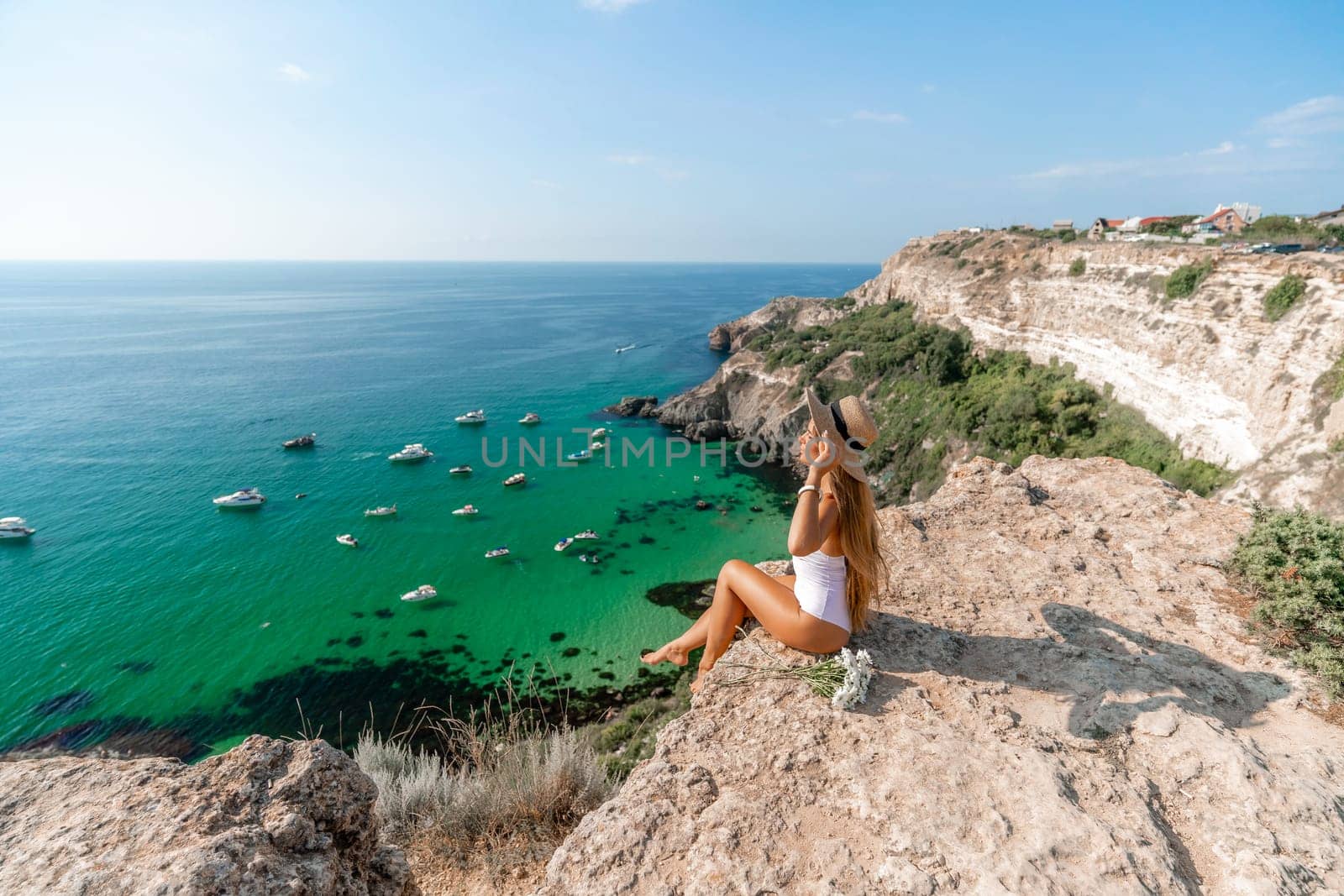 Woman travel sea. Happy woman in a beautiful location poses on a cliff high above the sea, with emerald waters and yachts in the background, while sharing her travel experiences.