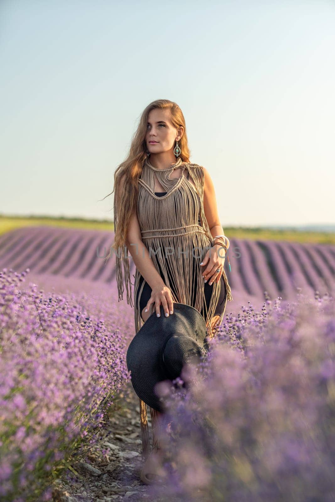 A woman is standing in a field of purple flowers, wearing a black dress and a black hat