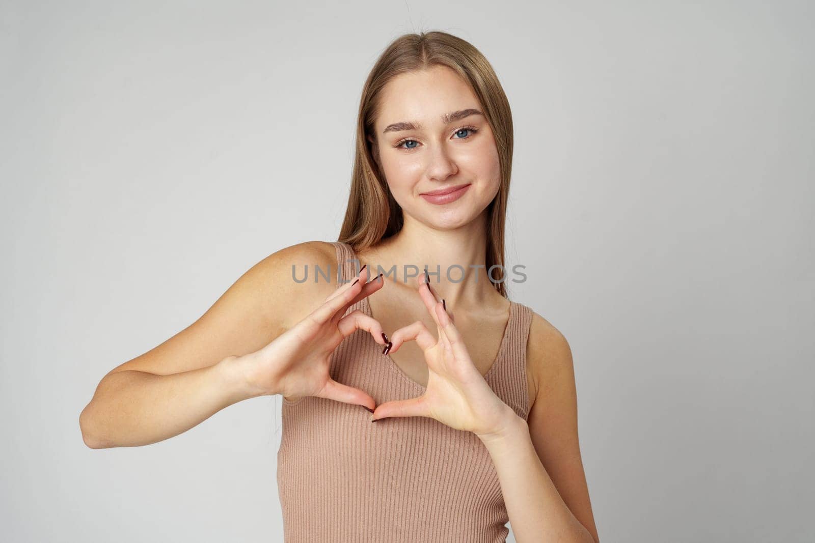 Smiling young woman showing heart with two hands on gray background by Fabrikasimf