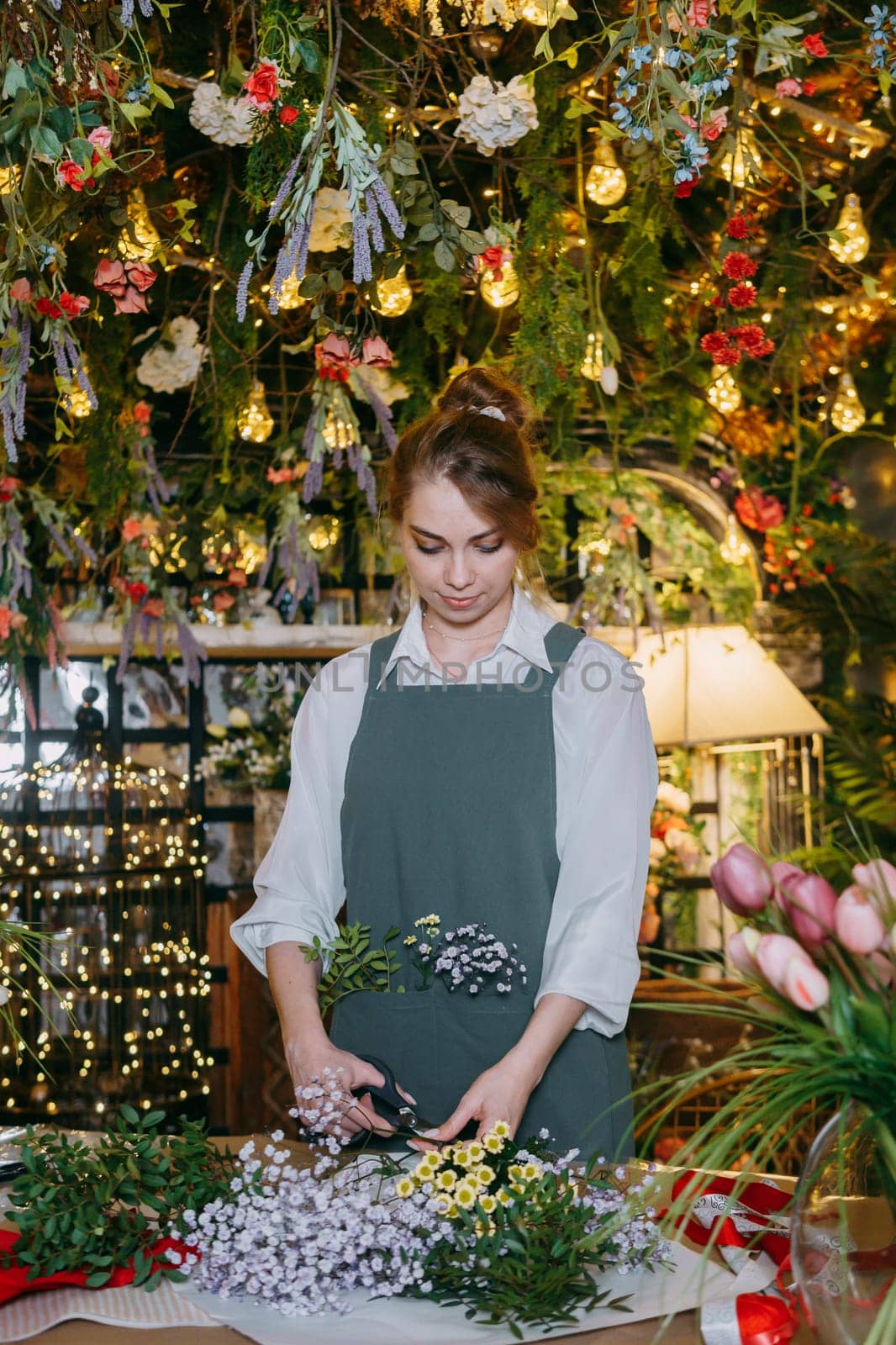 A woman in her florist shop collects bouquets of flowers. The concept of a small business. Bouquets of tulips for the holiday on March 8. by Annu1tochka