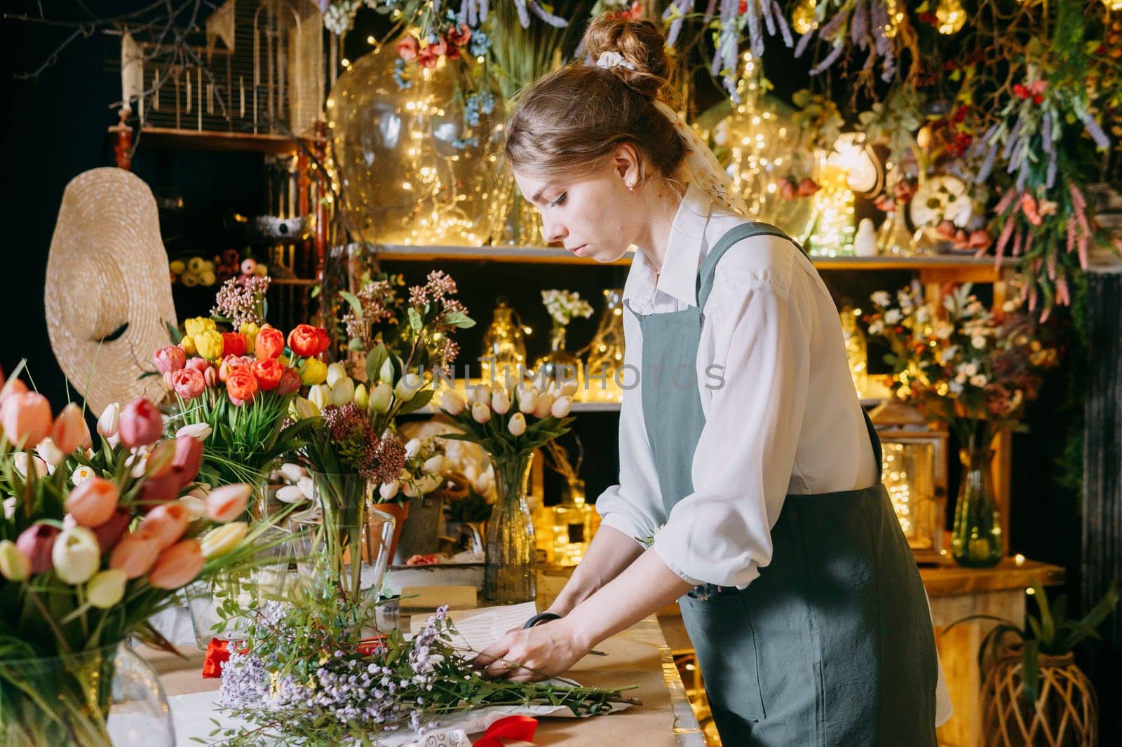 A woman in her florist shop collects bouquets of flowers. The concept of a small business. Bouquets of tulips for the holiday on March 8. by Annu1tochka