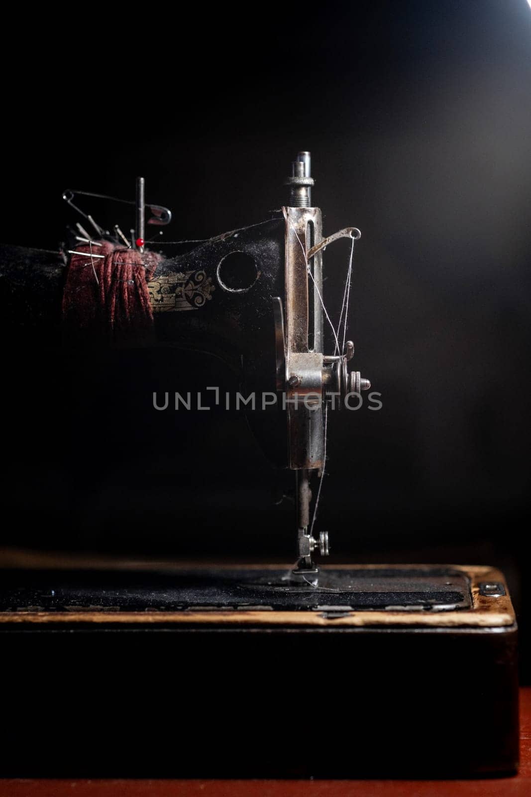 An old sewing machine stands on the table at home ready to work and sew. Classic retro style manual sewing machine ready for sewing work. The machine is old style made of metal with floral patterns