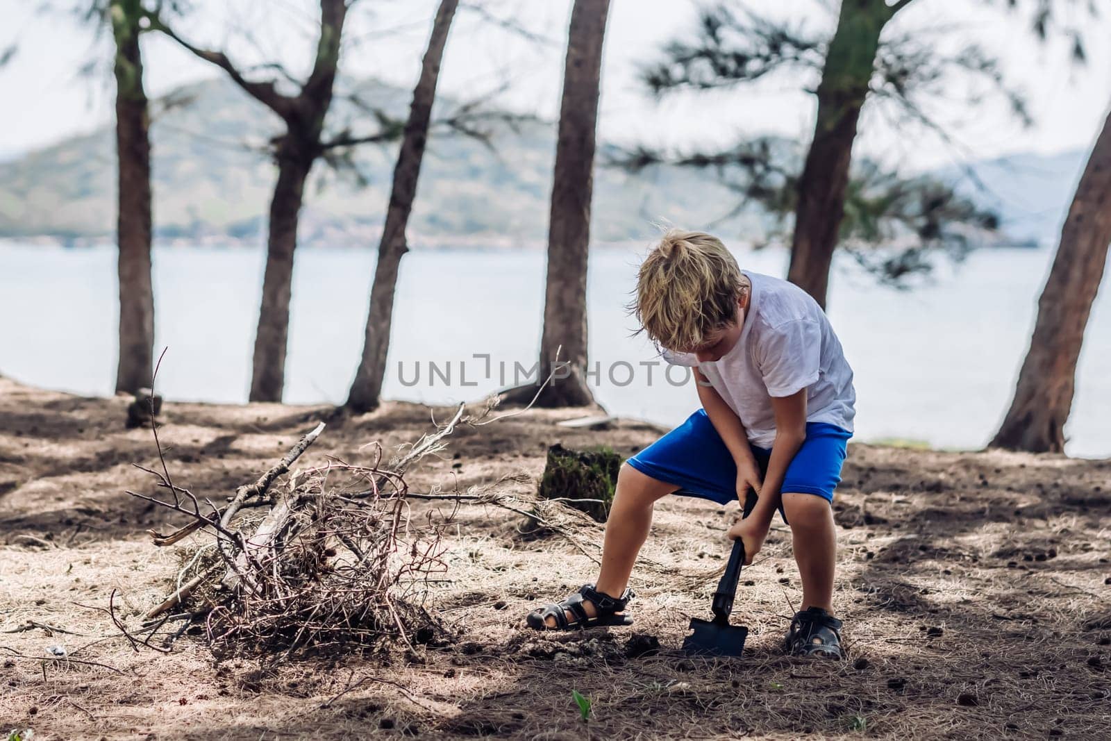 Cute boy digging soil in forest near sea beach. Family natural education skills. Travelling together. Learning camping organizing bonfire.