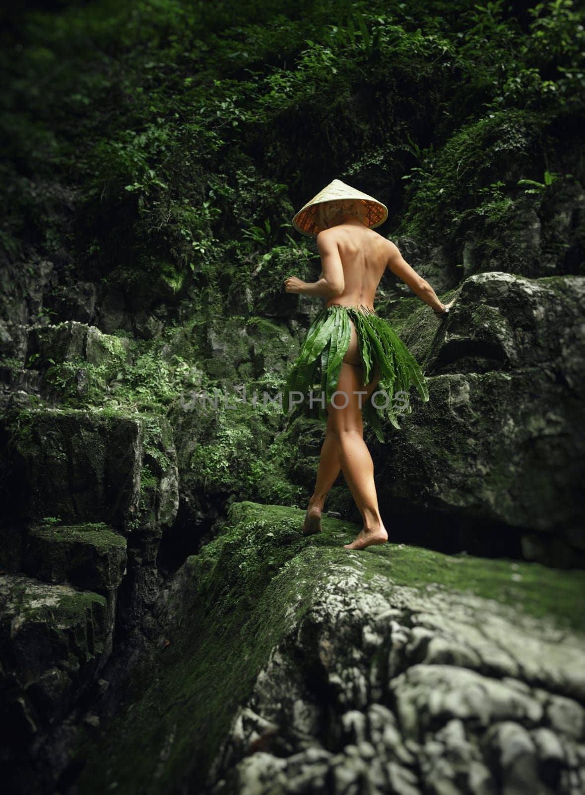 A naked sexy girl in a triangular Asian hat and a homemade cape made of leaves walks along the canyon of a mountain river by Rotozey