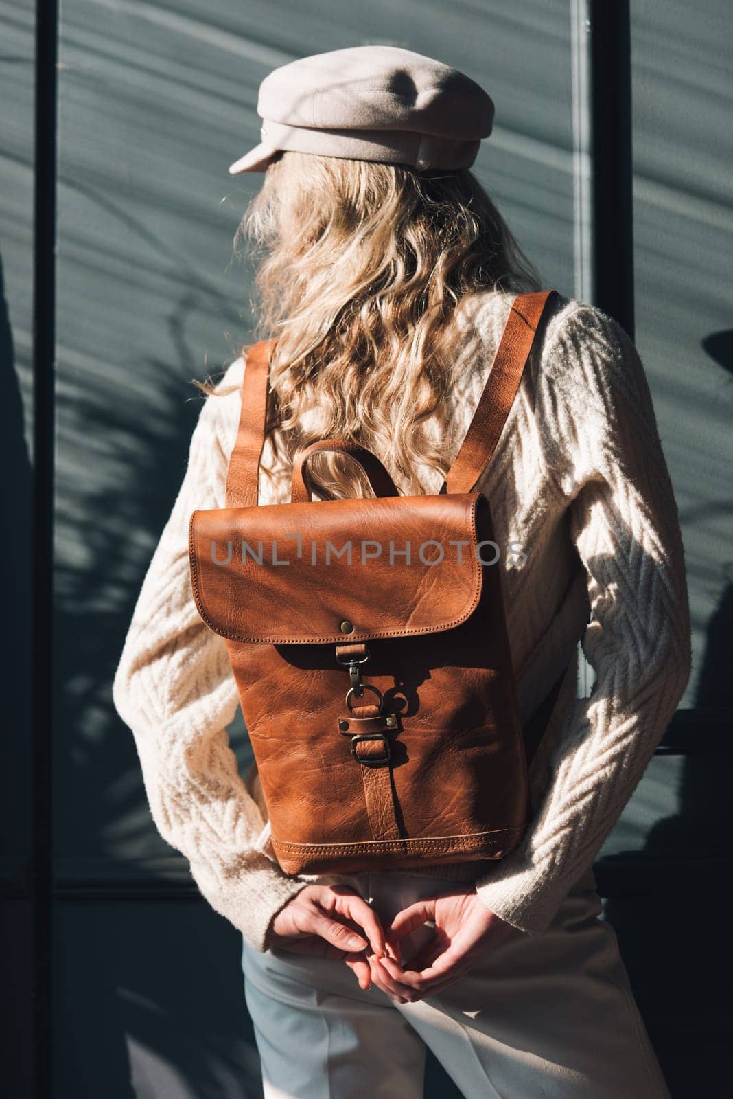 Studio portrait of beautiful woman with a curly blond hair holding brown backpack, posing on gray background. by Ashtray25