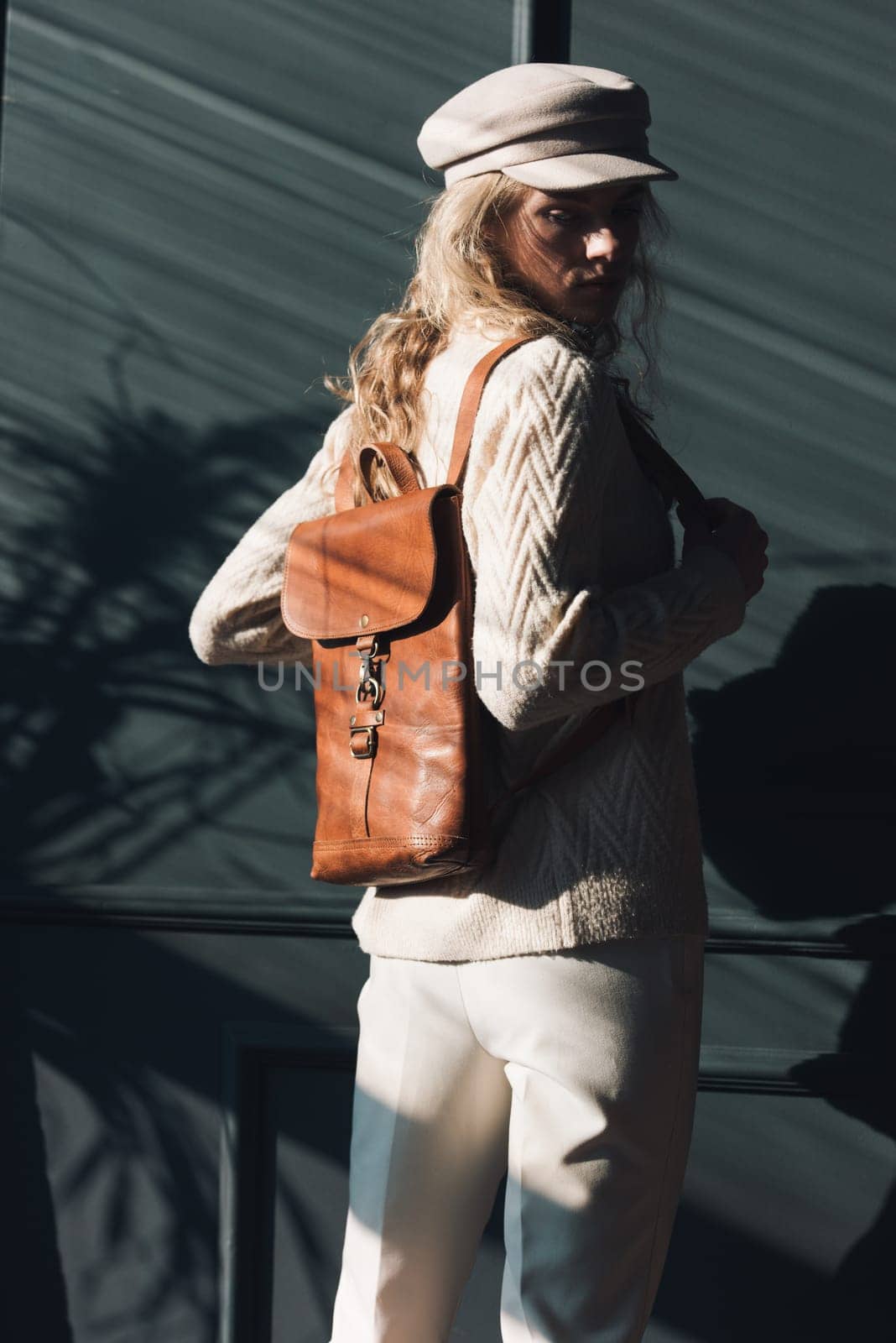 Studio portrait of beautiful woman with a curly blond hair holding brown backpack, posing on gray background. by Ashtray25