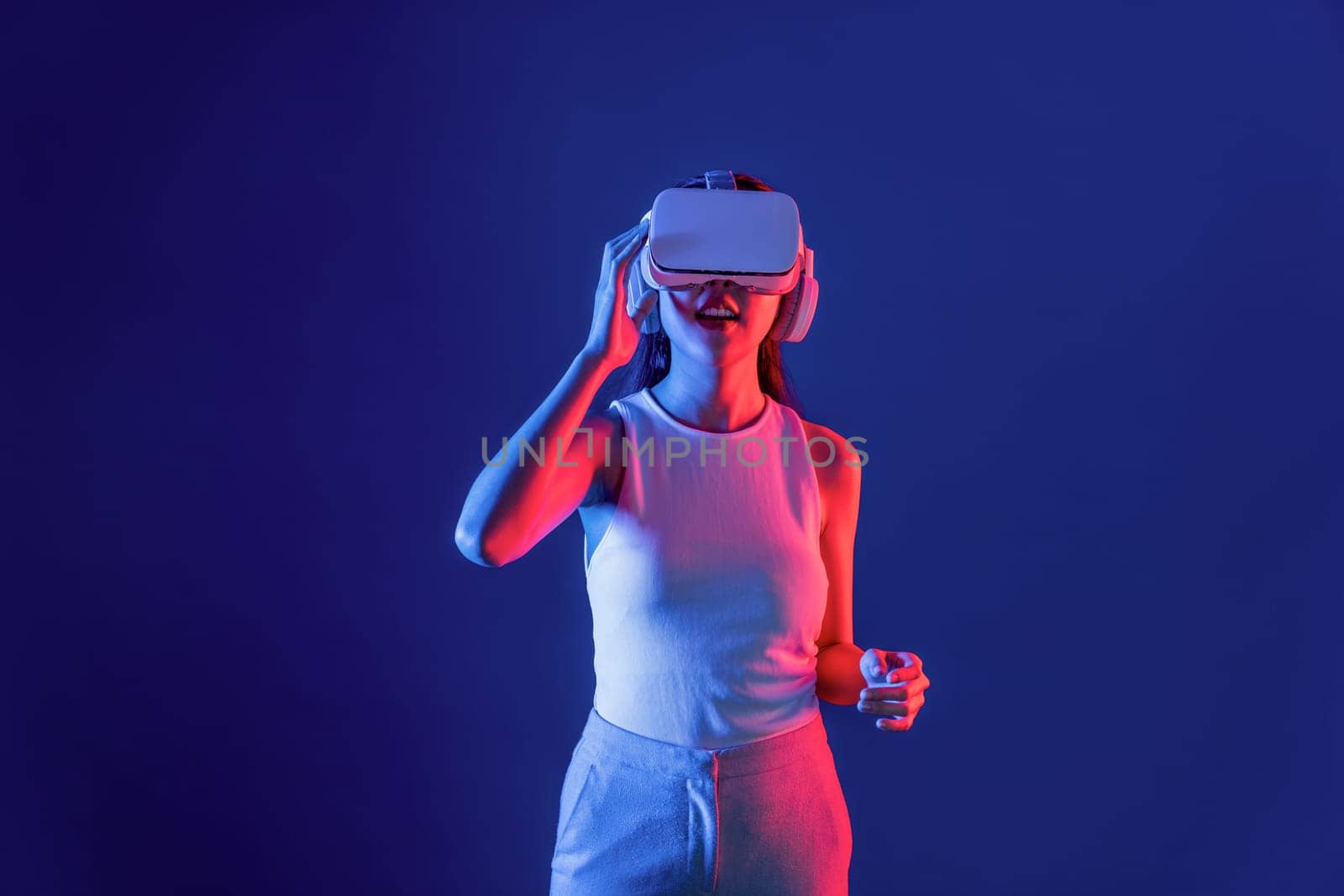 Smart female stand in cyberpunk neon light wearing VR headset connecting metaverse, futuristic cyberspace community technology. Elegant woman excited seeing generated virtual scenery. Hallucination.