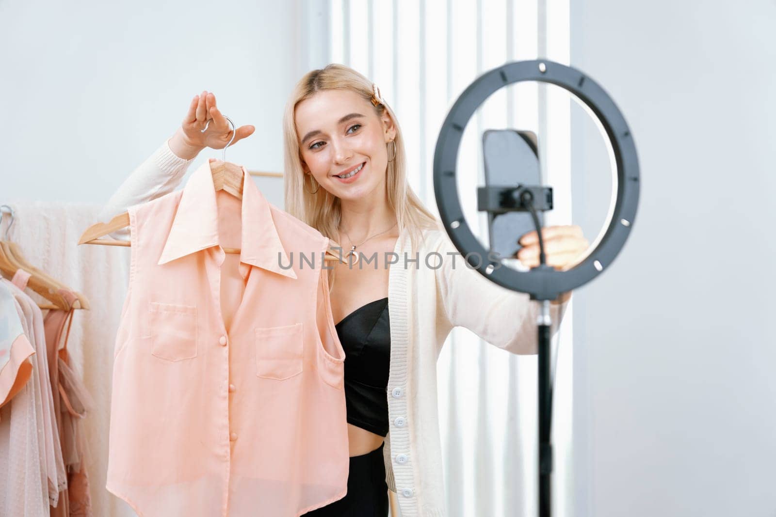 Young social medial content creator woman make fashion video. Blogger smiles to camera and light ring while making persuasive online clothing sell vlog to audience or follower. Blithe