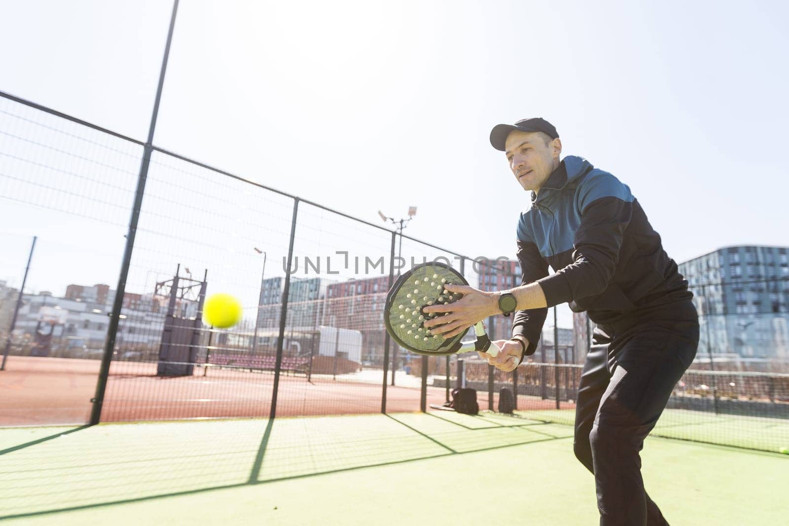 A padel player jump to the ball, good looking for posts and poster. Man with black racket playing a match in the open behind the net court outdoors. Professional sport concept with space for text. High quality photo